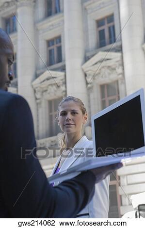 Side profile of a businessman using a laptop with a businesswoman standing in front of him View Large Photo Image Stock Image - Side profile of a businessman using a laptop with a businesswoman standing in front of him. Fotosearch