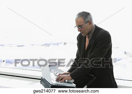 Side profile of a businessman using a laptop in the waiting room of an airport View Large Photo Image Stock Photo - Side profile of a businessman using a laptop in the waiting room of an airport. Fotosearch