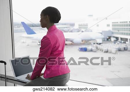 Stock Image - Side profile of a businesswoman using a laptop at an airport. Fotosearch