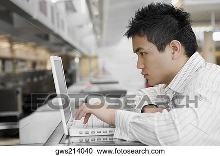Stock Image - Side profile of a young man using a laptop at an airport. Fotosearch