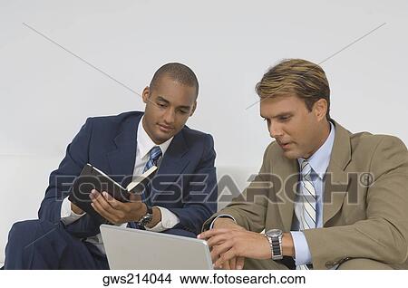 Picture - Two businessmen looking at a laptop and having a discussion. Fotosearch