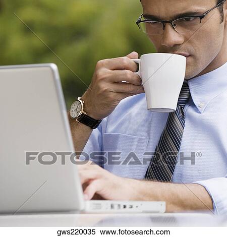 Close-up of a businessman drinking coffee while using a laptop View Large Photo Image Stock Photography - Close-up of a businessman drinking coffee while using a laptop. Fotosearch