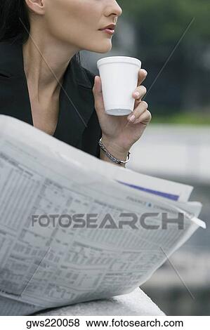 Stock Photo - Close-up of a businesswoman holding a disposable cup and a newspaper. Fotosearch