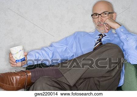Picture - Portrait of a businessman sitting in an armchair and holding a glass. Fotosearch
