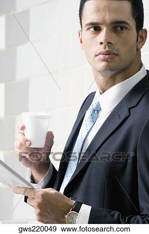 Side profile of a businessman holding a newspaper and a disposable cup View Large Photo Image Stock Photo - Side profile of a businessman holding a newspaper and a disposable cup. Fotosearch