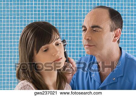Stock Image - Close-up of a male doctor examining a mature woman's ear. Fotosearch
