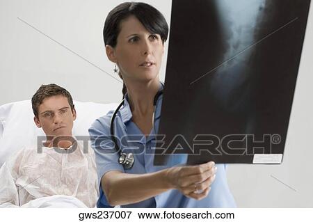 Female surgeon examining an X-Ray report with a patient in the background View Large Photo Image Stock Photo - Female surgeon examining an X-Ray report with a patient in the background. Fotosearch