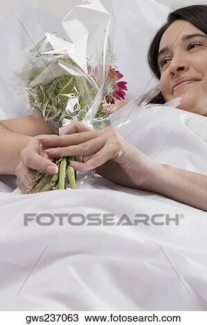 Stock Image - Patient lying on the bed and holding a bouquet of flowers. Fotosearch