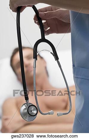 Surgeon holding a stethoscope with a patient in the background View Large Photo Image Stock Photo - Surgeon holding a stethoscope with a patient in the background. Fotosearch