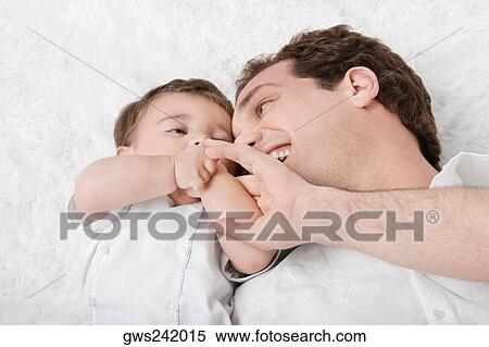 Close-up of a young man lying with his son View Large Photo Image Stock Photography - Close-up of a young man lying with his son. Fotosearch