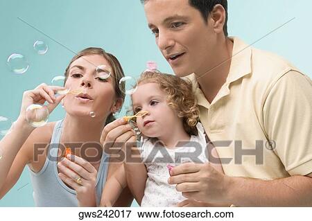 Stock Photo - Mid adult couple blowing bubbles with their daughter. Fotosearch