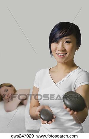 Close-up of a massage therapist holding two pebbles with a mature woman lying on a massage table behind her View Large Photo Image Stock Photo - Close-up of a massage therapist holding two pebbles with a mature woman lying on a massage table behind her. Fotosearch