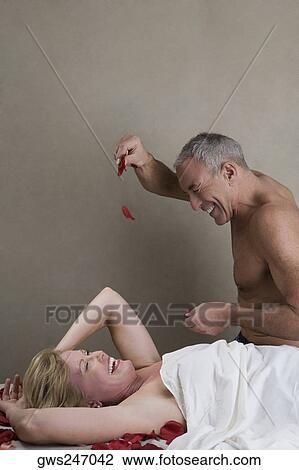 Stock Image - Side profile of a senior man throwing rose petals on a mature woman lying on a massage table. Fotosearch