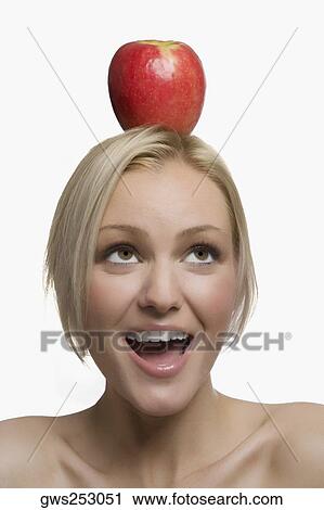 Stock Image - Close-up of a young woman balancing an apple on her head. Fotosearch