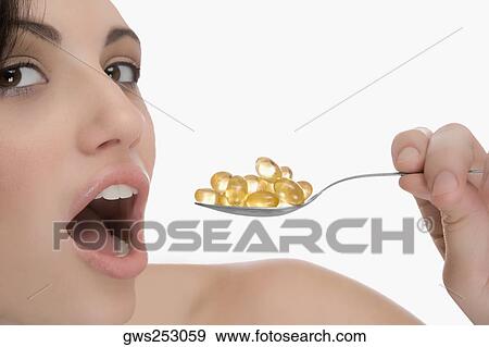 Stock Photo - Close-up of a young woman having pills from a spoon. Fotosearch