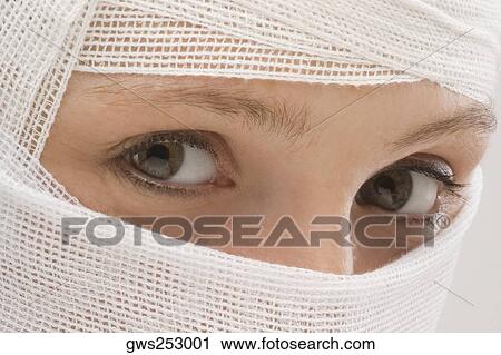 Stock Image - Close-up of a young woman's face wrapped with a bandage. Fotosearch