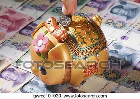 Stock Image - Close-up of a person's hand putting coin into a piggy bank. Fotosearch