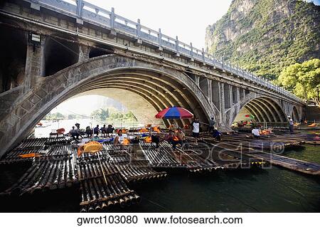 Tourists sitting on bamboo rafts under an arch bridge, Guilin Hills, XingPing, Yangshuo, Guangxi Province, China View Large Photo Image Stock Image - Tourists sitting on bamboo rafts under an arch bridge, Guilin Hills, XingPing, Yangshuo, Guangxi Province, China. Fotosearch