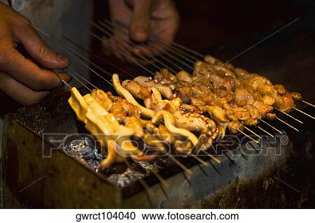 Stock Image - Close-up of a person's hands roasting seafood, Nanjing, Jiangsu Province, China. Fotosearch