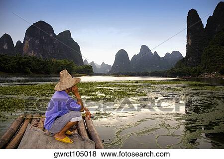 Stock Photo - Side profile of a mature man crouching on a bamboo raft with a hill range in the background, Guilin Hills, XingPing, Yangshuo, Guangxi Province, China. Fotosearch