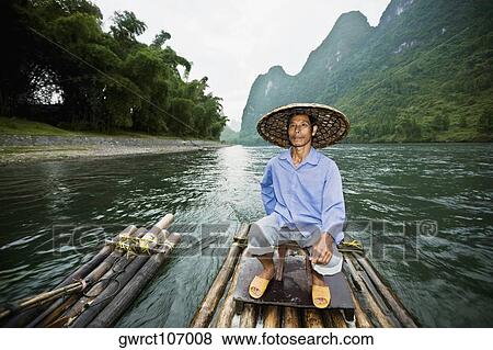 Mature man sitting on a wooden raft with a hill range in the background, Guilin Hills, XingPing, Yangshuo, Guangxi Province, China View Large Photo Image Stock Photo - Mature man sitting on a wooden raft with a hill range in the background, Guilin Hills, XingPing, Yangshuo, Guangxi Province, China. Fotosearch