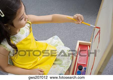 Stock Image - High angle view of a schoolgirl painting in an art class. Fotosearch