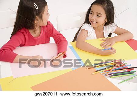 Stock Image - High angle view of two schoolgirls drawing together in a classroom. Fotosearch