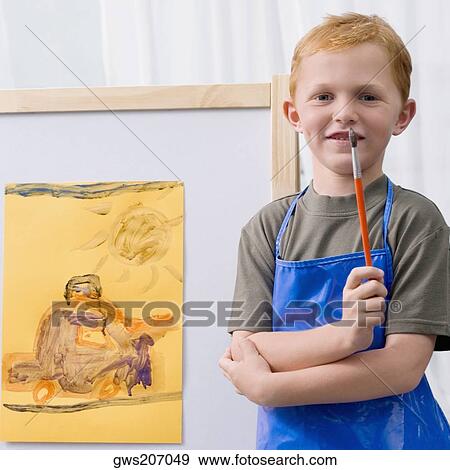 Stock Photo - Portrait of a schoolboy standing in front of his painting in a classroom. Fotosearch