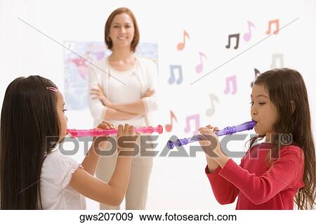 Side profile of two schoolgirls playing flutes with their teacher standing in the background View Large Photo Image Stock Photo - Side profile of two schoolgirls playing flutes with their teacher standing in the background. Fotosearch