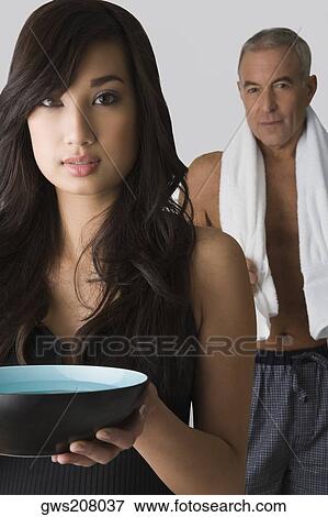 Portrait of a young woman holding a bowl and her father standing behind her View Large Photo Image Stock Photo - Portrait of a young woman holding a bowl and her father standing behind her. Fotosearch