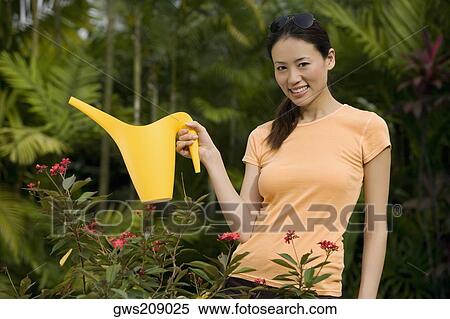 Stock Photography - Portrait of a young woman watering plant with a watering can and smiling. Fotosearch