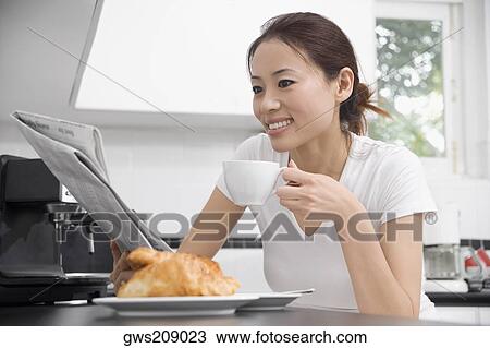 Stock Image - Young woman reading a newspaper and drinking tea. Fotosearch