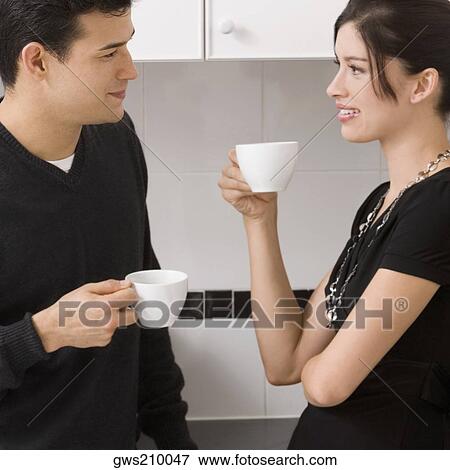 Stock Photo - Young couple holding cups of tea and looking at each other. Fotosearch