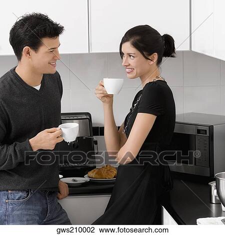 Young couple holding their coffee cups in the kitchen and smiling View Large Photo Image Stock Image - Young couple holding their coffee cups in the kitchen and smiling. Fotosearch