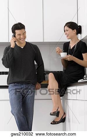 Young woman holding a tea cup with a young man talking on a mobile phone View Large Photo Image Stock Image - Young woman holding a tea cup with a young man talking on a mobile phone. Fotosearch