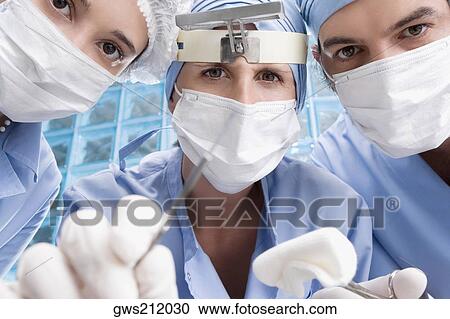 Stock Image - Close-up of two female surgeons and a male surgeon in an operating room. Fotosearch