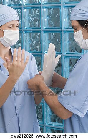 Stock Photograph - Male surgeon adjusting a surgical glove of a female surgeon. Fotosearch