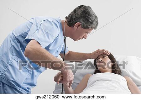 Stock Image - Side profile of a male surgeon examining a young woman. Fotosearch