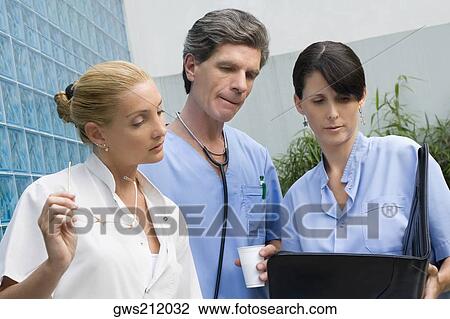 Stock Image - Two female surgeons and a male doctor discussing a medical report. Fotosearch