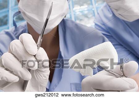 Stock Image - Two surgeons holding a scalpel and a surgical scissors. Fotosearch
