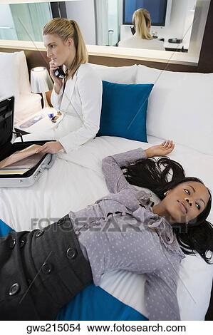 Businesswoman talking on a cordless phone and another businesswoman lying on the bed View Large Photo Image Picture - Businesswoman talking on a cordless phone and another businesswoman lying on the bed. Fotosearch