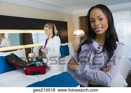 Stock Photo - Portrait of a businesswoman smiling with another businesswoman packing her luggage. Fotosearch