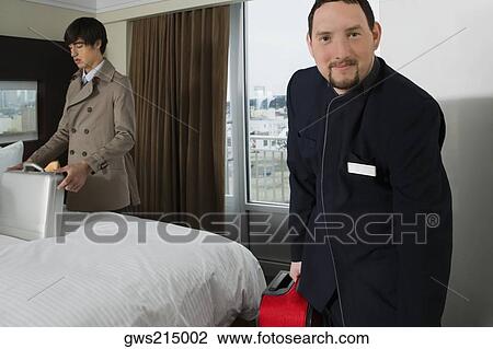 Portrait of a room service man holding a luggage with a businessman looking at a briefcase View Large Photo Image Stock Image - Portrait of a room service man holding a luggage with a businessman looking at a briefcase. Fotosearch