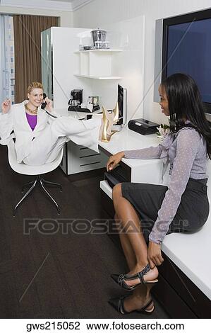 Stock Image - Two businesswomen looking at each other and smiling. Fotosearch