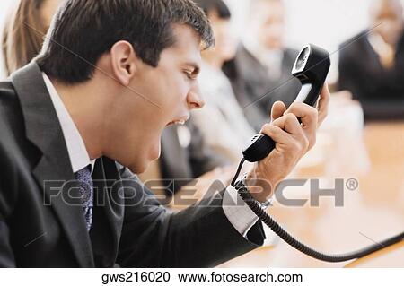 Stock Image - Close-up of a businessman shouting in front of a telephone receiver. Fotosearch
