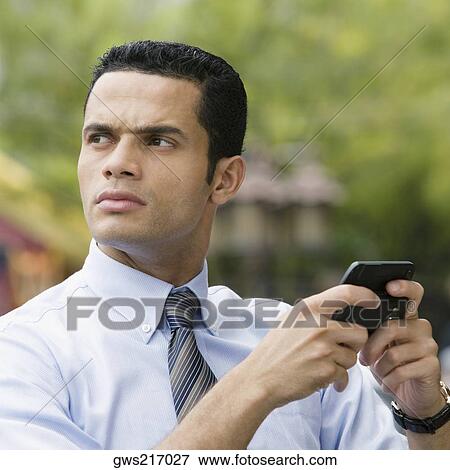 Stock Photo - Close-up of a businessman using a personal data assistant and thinking. Fotosearch
