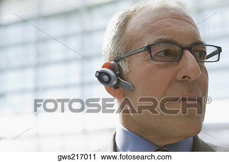 Stock Image - Close-up of a businessman wearing a bluetooth and looking away. Fotosearch