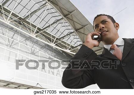 Low angle view of a businessman talking on a mobile phone outside an airport View Large Photo Image Stock Photography - Low angle view of a businessman talking on a mobile phone outside an airport. Fotosearch