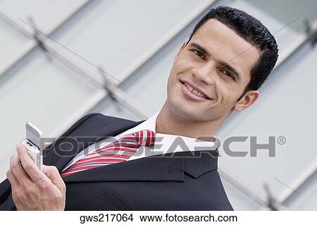 Portrait of a businessman holding a mobile phone and smiling View Large Photo Image Picture - Portrait of a businessman holding a mobile phone and smiling. Fotosearch
