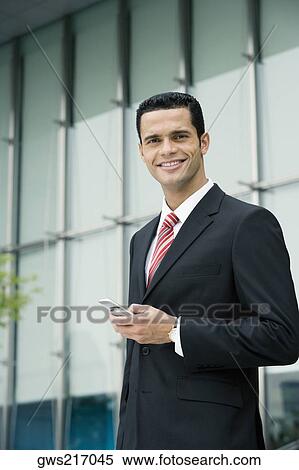 Portrait of a businessman holding a mobile phone and smiling View Large Photo Image Stock Photography - Portrait of a businessman holding a mobile phone and smiling. Fotosearch